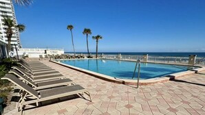 A pool area with lounge chairs, palm trees, and a clear view of the ocean. - Beautiful 9th floor OceanView Studio Condo  - Pool is OPEN! (Daytona Beach)