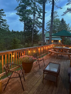 A wooden deck with outdoor seating, a potted plant, and string lights. - As featured in the NY Times: charming, home on Lake Rescue, minutes from Okemo. (Ludlow)