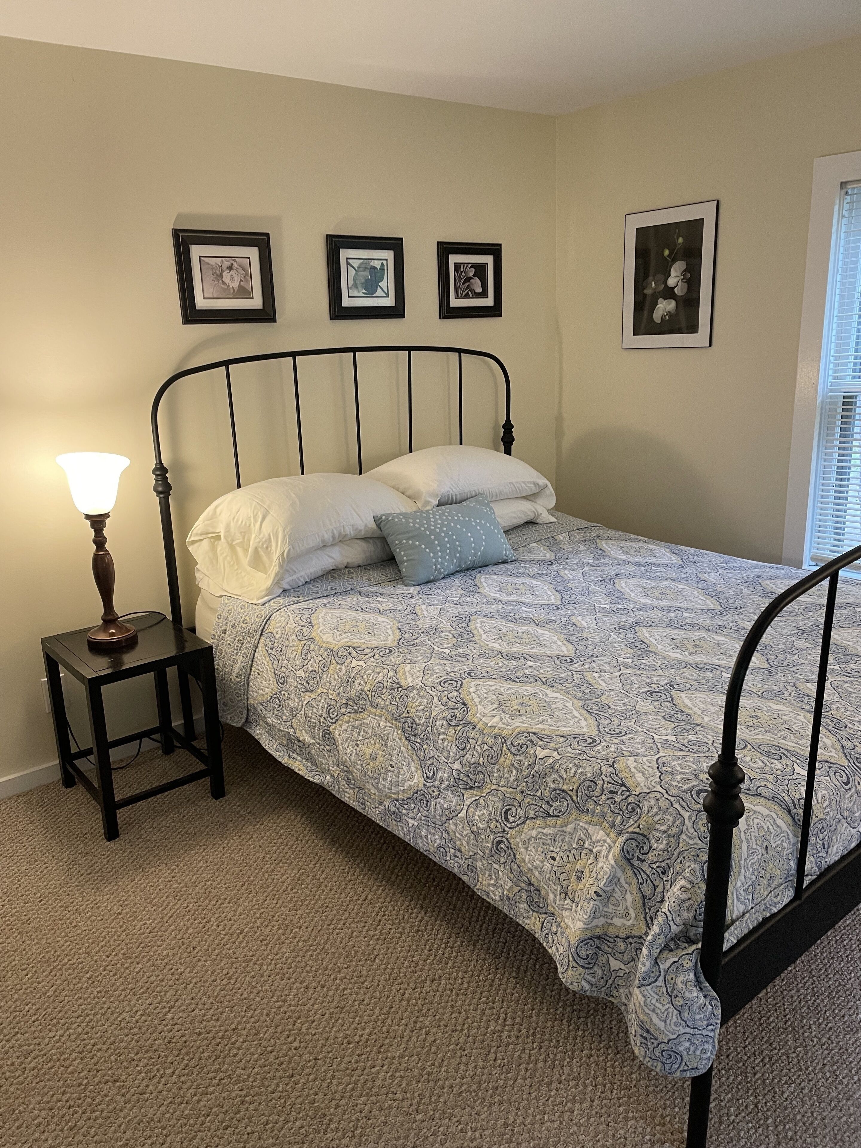 A bedroom with a bed, a nightstand, and a lamp. There are three framed pictures on the wall.