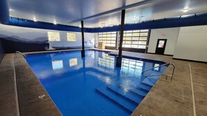 An indoor swimming pool with clear water, a wooden deck surrounding it, and a mural on the wall depicting a mountain landscape.