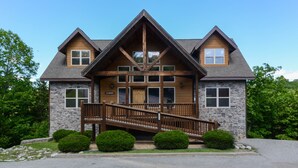 A two-story lodge with a stone facade, wooden trim, and a central staircase leading to a deck.