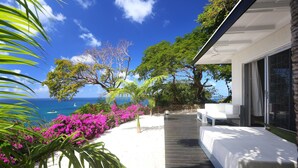 A modern outdoor seating area with a view of the ocean, surrounded by lush greenery and vibrant flowers. - Ultimate Caribbean Getaway: 3 beaches, Cook, Housekeeper & Valet, 24x7 Concierge (Gros Islet)