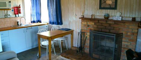 Una cocina acogedora con una mesa de madera, sillas blancas, una chimenea de ladrillo y una ventana con cortinas azules.