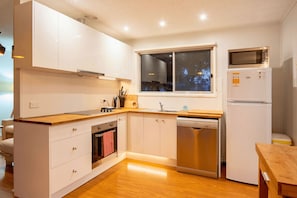 Una cocina compacta con armarios blancos, encimera de madera, horno integrado, lavavajillas y microondas.
