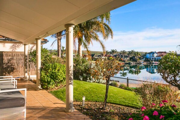 A covered outdoor area with a pool, palm trees, and a view of a residential area.