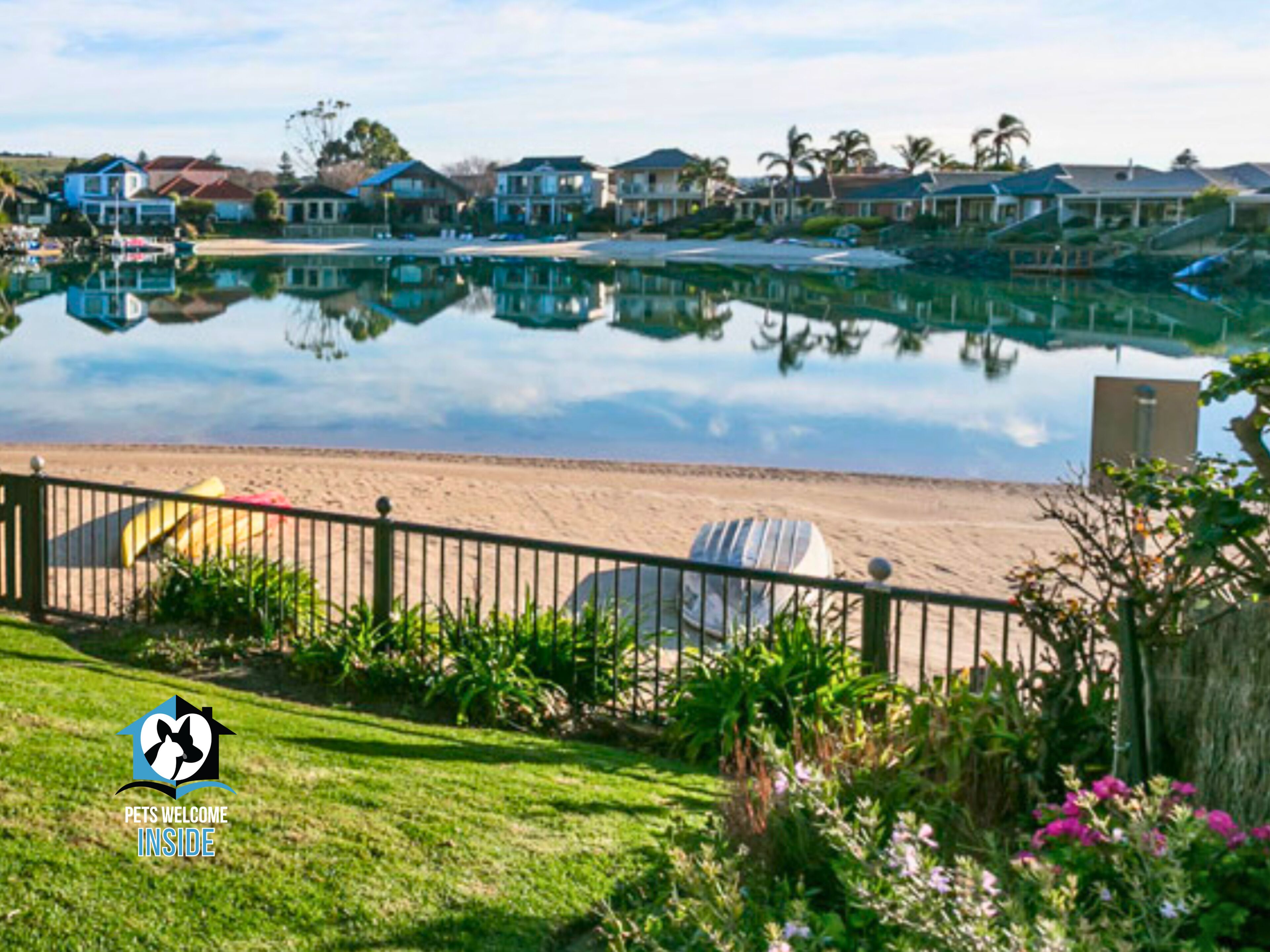 A beachfront property with a pool, a fenced area with beach chairs, and a logo indicating pet-friendly accommodation.