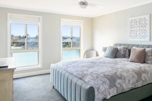 A bedroom with a large bed, two windows, a ceiling fan, and a decorative wall piece.