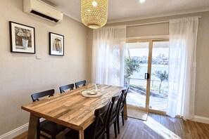 A dining area with a wooden table, chairs, a hanging light fixture, and a view through a glass door.