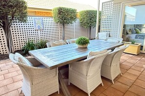 A rectangular outdoor dining table with six chairs, surrounded by a white lattice fence, and a potted plant on the table.