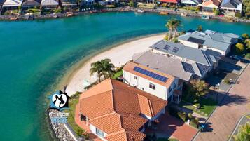 An aerial view of a coastal residential area with houses, a beach, and a clear blue sea.