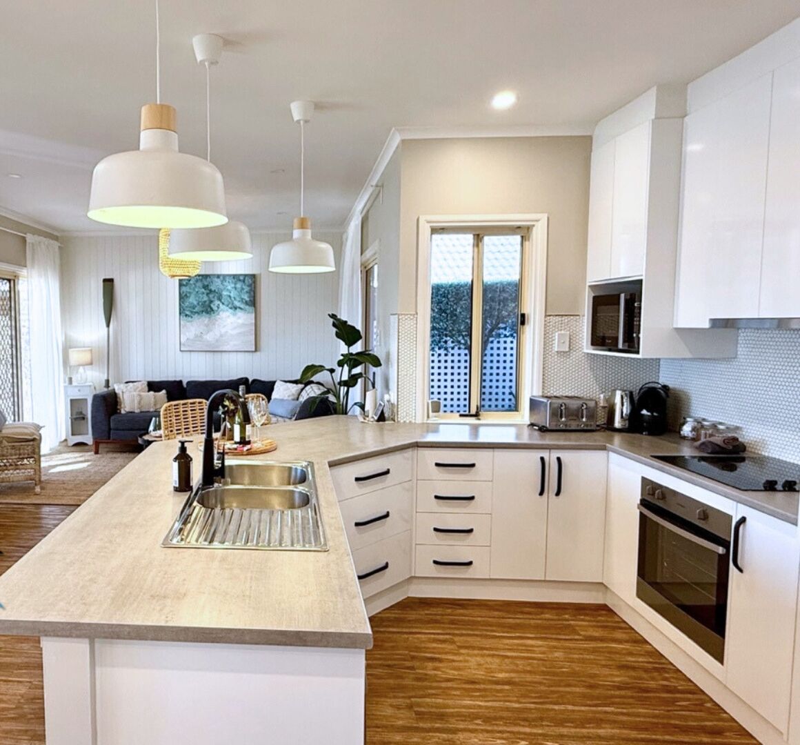 A modern kitchen with a central island, white cabinetry, and a large window.