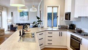 A modern kitchen with a central island, white cabinetry, and a large window. - Holiday Home with Private Beach & Stunning Views! (Encounter Bay)