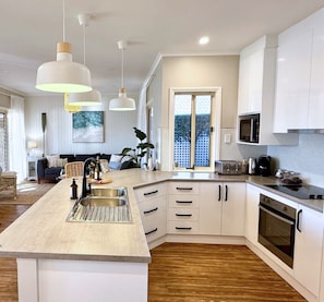 A modern kitchen with a central island, white cabinetry, and a large window. - Holiday Home with Private Beach & Stunning Views! (Encounter Bay)