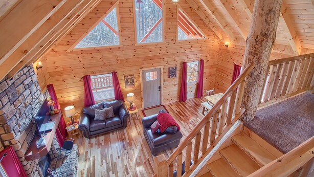 Ein Holzblockhaus-Interieur mit Steinwand, Kamin, Sofa, Esstisch und einer Treppe.