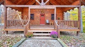 Eine Blockhütte mit Veranda, einer roten Tür und einem Kranz darüber.