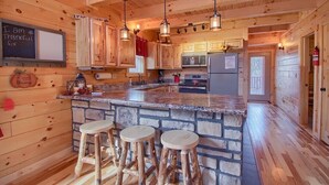 Ein Holzblockhaus-Innenraum mit Küchenbereich, der eine Steininsele, Barhocker, Holzausstattung und eine Tafel mit einer Botschaft zeigt.