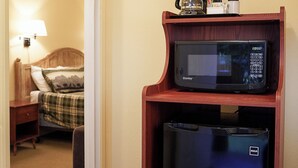 A hotel room with a microwave on a wooden shelf, a refrigerator below it, and a bed with a lamp in the background. - Emerald Room At Forest House (Pre-packed Breakfast Inc., 1mile from Mt Rainier) (Ashford)