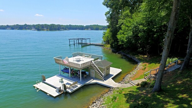 A floating deck with a covered seating area and a small cabin, surrounded by water and greenery. - Charming waterfront home, with central location to area marinas, plus Super Dock (Moneta)