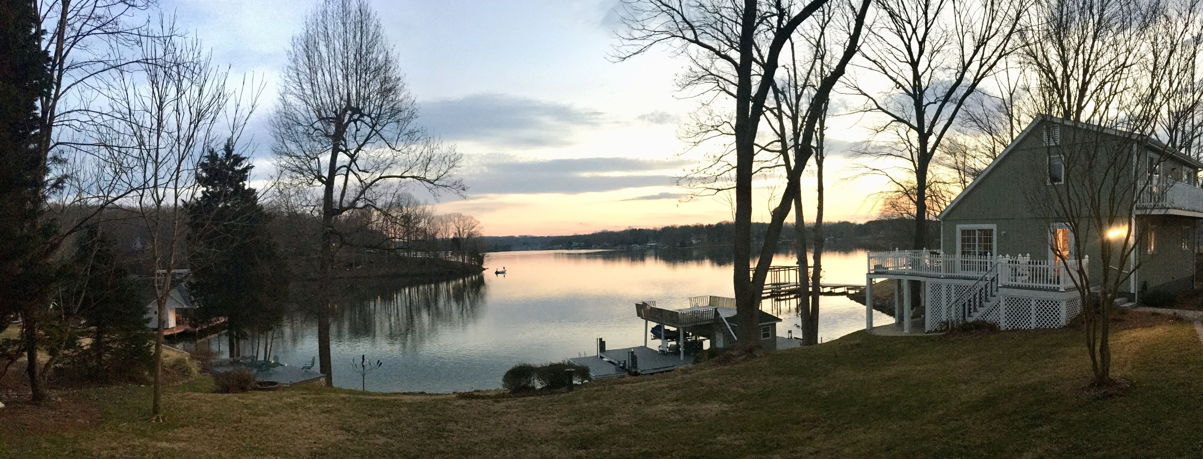 A lakeside property with a dock, a wooden deck, and a house with a white fence.