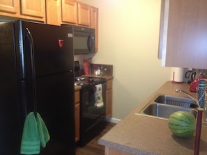 A kitchen with wooden cabinets, a black refrigerator, a microwave, an oven, a sink, and a countertop with a watermelon. - An Apartment Gem Located In The Heart Of Missoula (Missoula)
