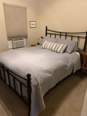 A neatly made bed with a quilted cover, a bedside table with a lamp, and a wall-mounted air conditioner. - An Apartment Gem Located In The Heart Of Missoula (Missoula)