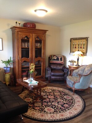 A living room with a wooden cabinet, a blue armchair, a brown leather chair, a round rug, and a small table with a vase. - An Apartment Gem Located In The Heart Of Missoula (Missoula)