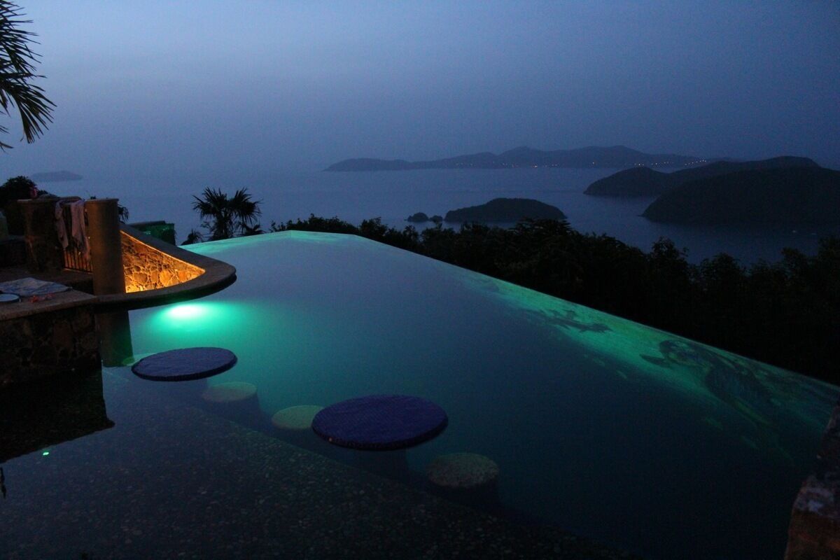 A infinity pool with a view of the sea and islands at dusk.