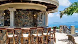 Zona de bar al aire libre con paredes de piedra y vistas al mar.