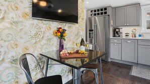 A modern kitchen with a flat-screen TV, a stainless steel refrigerator, and a dining area with a glass table and chairs.