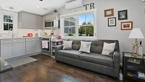 A modern kitchen with grey cabinets, a grey sofa, and a dining area.