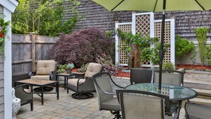 An outdoor patio area with wicker furniture, a glass table, and a green umbrella.