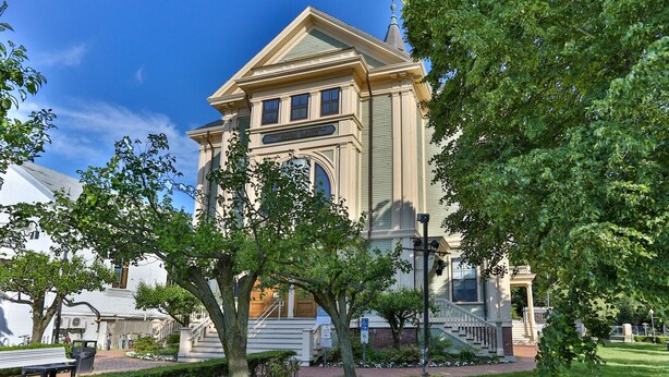 A historic building with a prominent entrance, a staircase, and a well-maintained lawn.