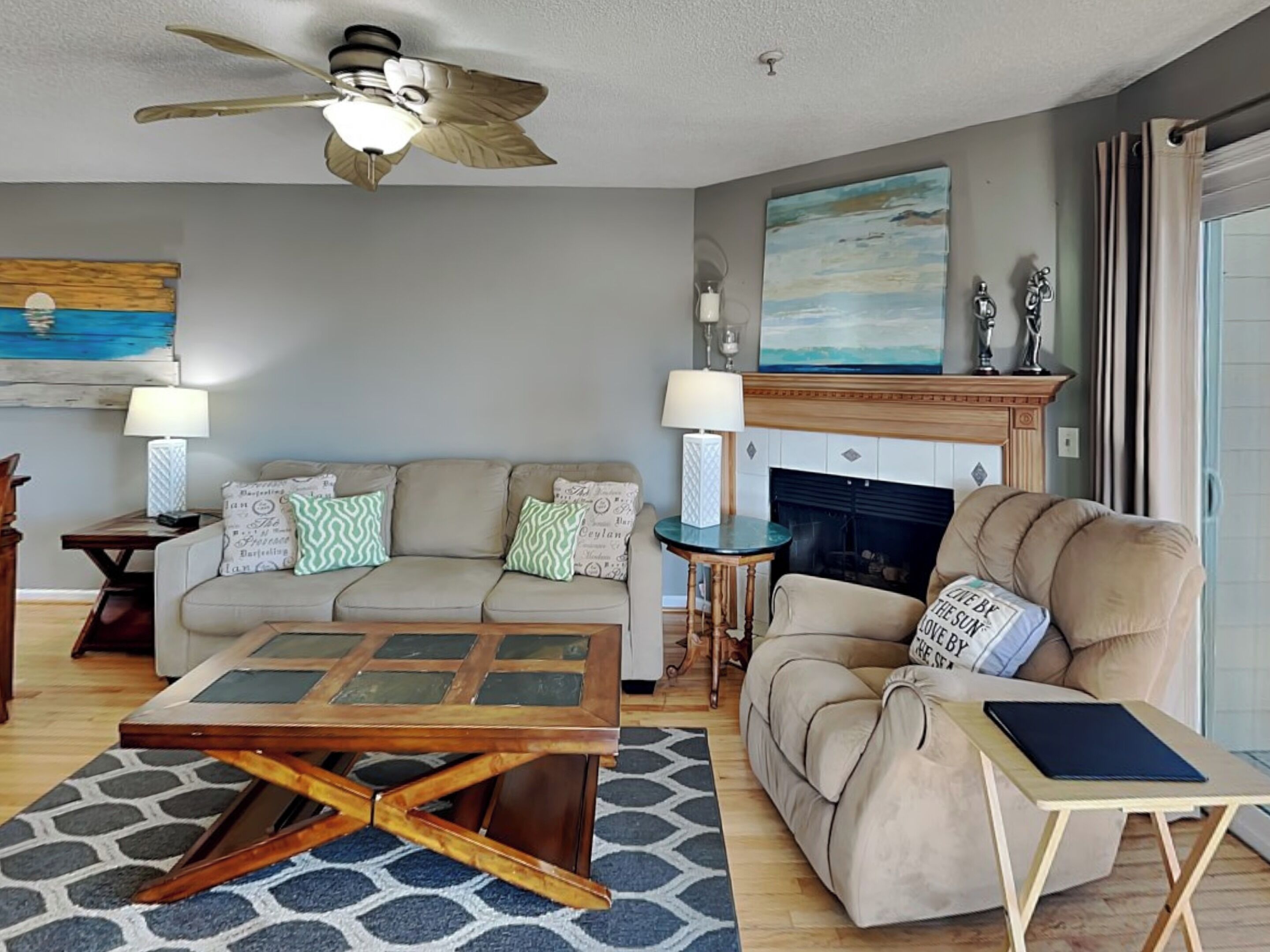 A living room with a sofa, armchair, coffee table, fireplace, and ceiling fan.