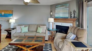 A living room with a sofa, armchair, coffee table, fireplace, and ceiling fan.