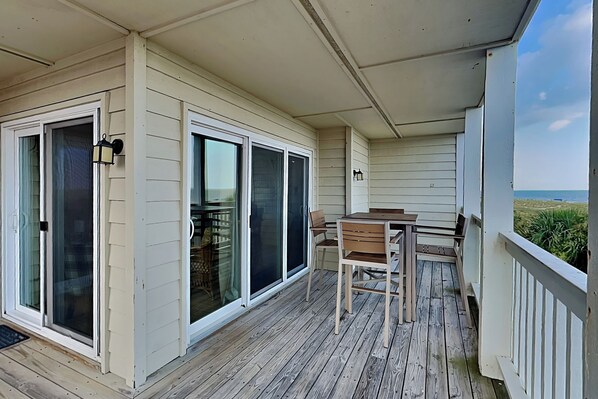 A covered outdoor area with a table and chairs, sliding glass doors, and a view of the ocean.