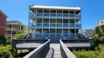 A multi-story building with balconies and a wooden boardwalk leading to it.