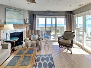 A spacious living room with a fireplace, a comfortable armchair, a sofa, and a view of the ocean through large windows.