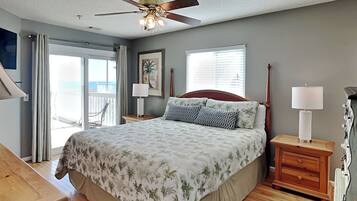 A bedroom with a bed, a ceiling fan, a nightstand with a lamp, a wooden dresser, and a view of the outdoors through a sliding door.