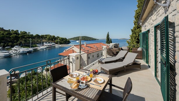 A balcony with a table set for breakfast overlooking a marina with boats and a clear view of the sea.