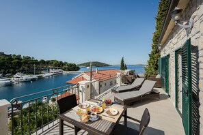 A balcony with a table set for breakfast overlooking a marina with boats and a clear view of the sea.