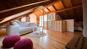 An attic room with a white sofa, a small table, and two pink poufs.