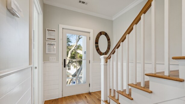 A hallway with a wooden staircase, white walls, and a door leading outside.