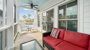 A covered outdoor area with a red sofa, a ceiling fan, and a view of palm trees.
