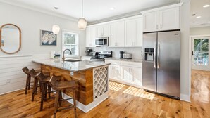 A modern kitchen with white cabinets, stainless steel appliances, a wooden island with bar stools, and a large refrigerator.