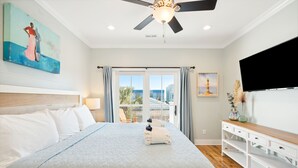 A bedroom with a large bed, a ceiling fan, a TV, and a view of the outdoors.