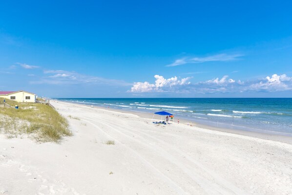 A beach with a white building, a blue umbrella, and the ocean. - Paradise Found - Updated Classic 3 BR Home - Direct Oceanfront! (North Topsail Beach)