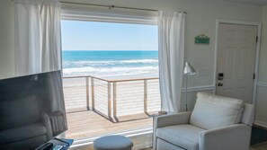 Een kamer met uitzicht op de oceaan, een witte stoel, een televisie en een deur met een bordje.