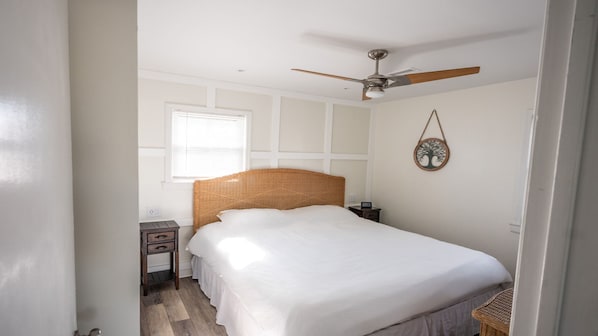Een slaapkamer met een groot bed, een plafondventilator, een nachtkastje en een decoratie aan de muur.