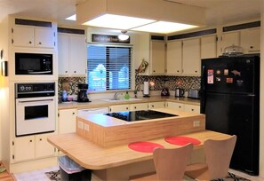 A compact kitchen with white cabinets, a black refrigerator, a microwave, an oven, a coffee maker, and a sink.