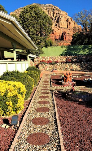 Un camino con placas metálicas decorativas, un muro de piedra y un edificio con tejado verde.